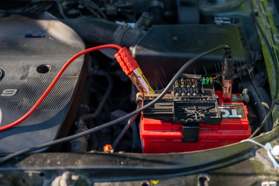 Red jumper cable clamps connected to a car battery under the hood for an emergency jumpstart